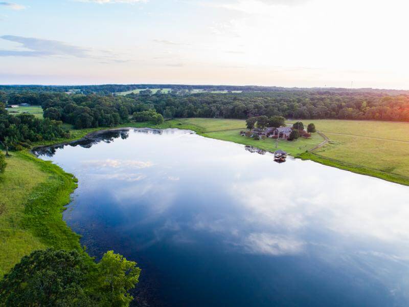 House by large manmade lake with green pastures surrounding the house